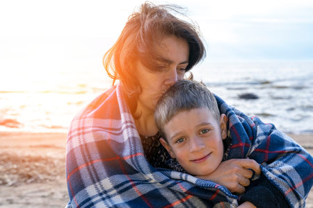 mother and her son are relaxing on the beach wrapped in a plaid plaidの写真素材