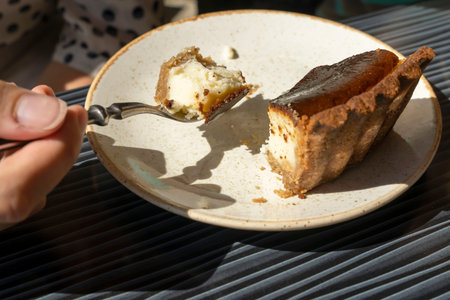 womans hand with a spoon takes a piece of cheesecake from a plate