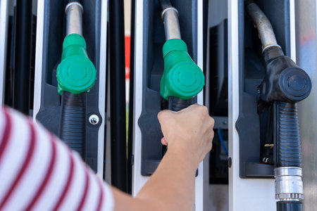 a womans hand removes a refueling gun from the pump to refuel the car