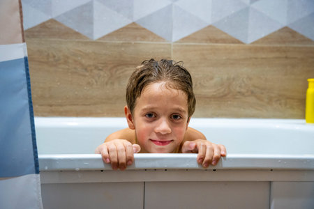 preschooler boy washes his head with his hands in the bathroom with shampoo