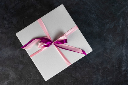 white cardboard gift box tied with a red ribbon on a dark background