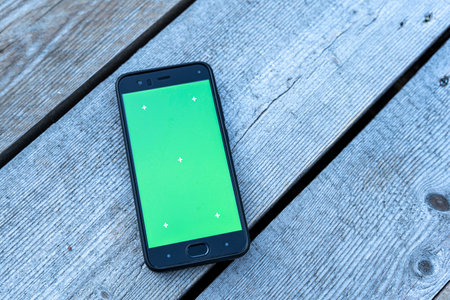 a smartphone with a green screen lies on a faded wooden backgroundの写真素材