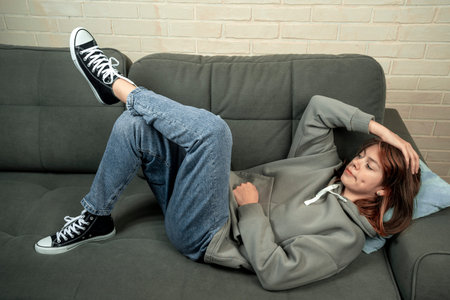 A happy relaxed Caucasian girl is resting, lying on a comfortable sofa