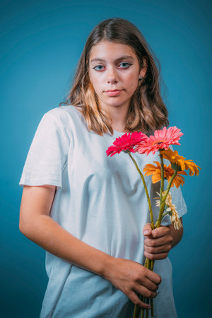 portrait of a pretty Caucasian girl with gerbera flowers on a blue backgroundの写真素材