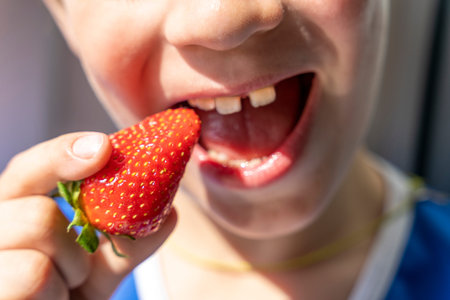 boy takes a bite out of a red strawberry berry