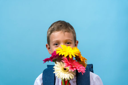 a funny first grader in a white shirt with a backpack holds a bouquet of flowers in his hands and...