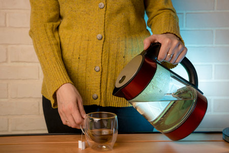 woman pouring hot water from a kettle into a clear glass mugの写真素材