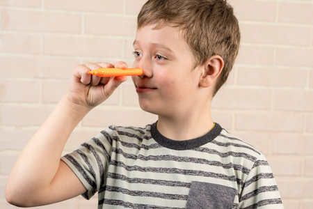 boy is fooling around by putting an orange marker to his noseの写真素材