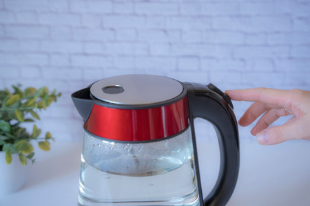 electric kettle with boiling water and a hand pressing the off buttonの写真素材
