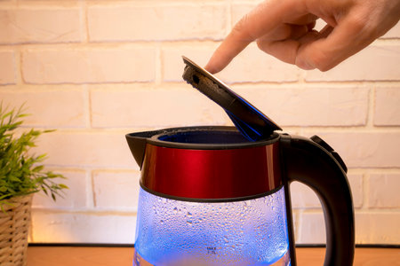 kettle with boiling water and a person s finger closes the lidの写真素材