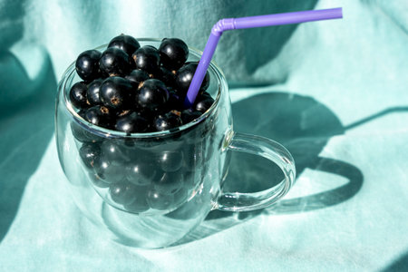 Summer fresh black currant berries in a glass mug with a cocktail tubeの写真素材