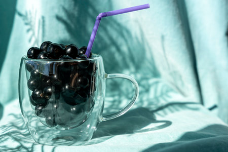 Summer fresh black currant berries in a glass mug with a cocktail tubeの写真素材