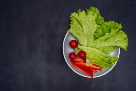 plate with green lettuce leaves and tomato and pieces of fresh sweet pepperの写真素材