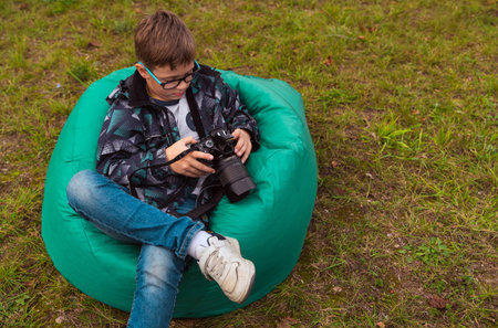 a boy with a camera is sitting on a green comfortable bag chair on the grassの写真素材