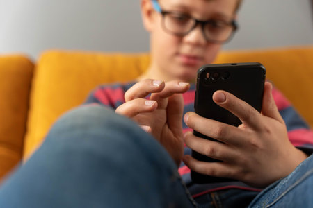 boy is sitting on the couch and using a smartphone