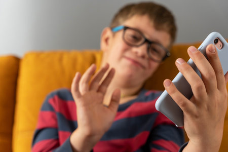 boy is sitting on the couch and communicating with his grandmother via videoの写真素材