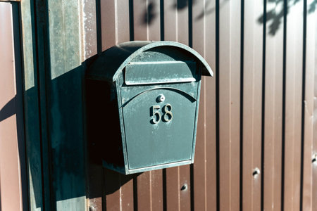 A classic red mailbox stands at the gate of a charming private house in a quiet suburban neighborhood, surrounded by lush greenery and a serene atmosphere.の写真素材
