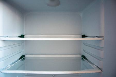Close-up of modern, spacious refrigerator with empty glass shelves, showing the interior organizer and ample storage space for groceries and beverages in a clean, well-lit kitchen setting.の写真素材