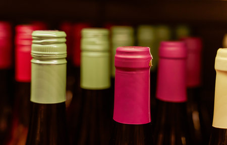 An arrangement of wine bottles on a store shelf, adorned with eye-catching green and pink caps, presenting an assortment of alcoholic drinks suitable for festive occasions and holiday gatherings.の写真素材