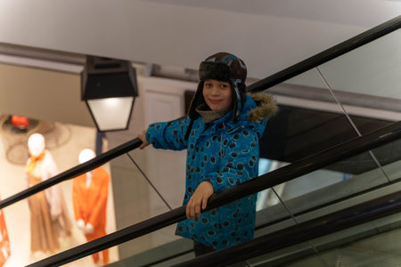 A boy wearing a blue jacket and a hat is standing on an escalatorの写真素材
