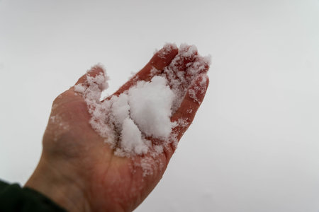 A man's hand holds snow in the palm of his hand.