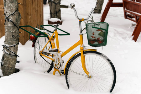 A snowy parking lot with a scenic view of a yellow classic ladies' bicycle with a basket, covered in snow. The serene winter landscape is perfect for outdoor and lifestyle themes.の写真素材