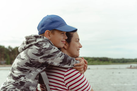 Family Bonding: Son Hugging Mother in Affectionate Embrace at Lake Camping Tripの写真素材
