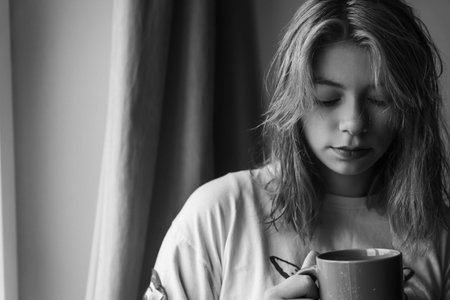 A youthful girl from Generation Z, with stunning red hair, sits by the window, savoring a hot cup of tea or coffee. The peaceful ambiance and her serene expression make for a compelling scene.の写真素材
