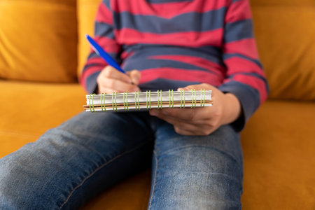 Rest between classes. boy draws in a notebook while sitting on sofa. Homeworkの写真素材