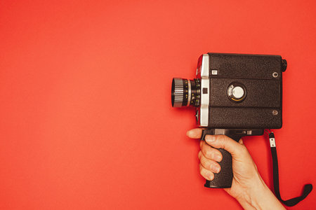 vintage portable movie camera in a womans hand on a red background