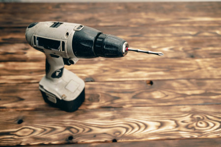 There is a cordless drill on a wooden table. A working tool. DIY concept