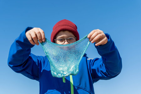 A boy holds up a piece of slime in front of his faceの写真素材