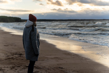 a woman stands on the seashore in the cold during a storm.の写真素材