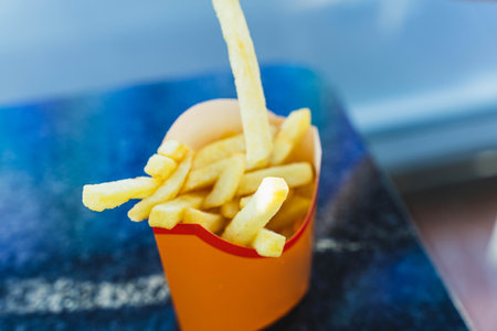 Crispy and Delicious Golden French Fries Served in a Paper Cup on a Wooden Tableの写真素材