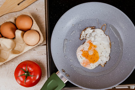 Frying eggs and tomatoes in a pan on a kitchen counter. rustic breakfastの写真素材