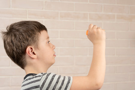 A school-age boy writes words on an invisible wall with a markerの写真素材