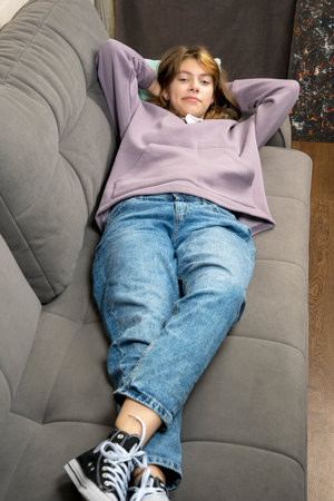 a teenage girl is lying on the couch with her hands behind her head.の写真素材