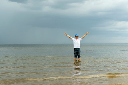 a happy boy stands in the water in the sea and raises his hands upの写真素材