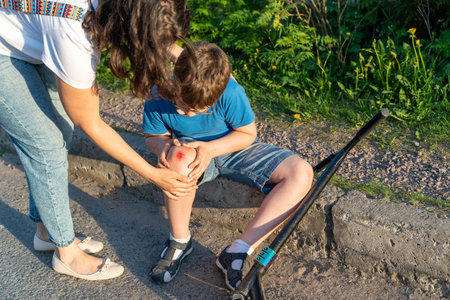 A mother comforts her son after he fell off his scooter while on vacationの写真素材