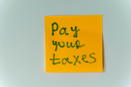 A yellow sticky note with the handwritten message Pay Your Taxesの写真素材