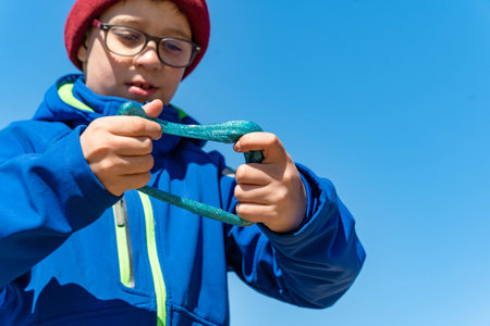 A young boy joyfully holds a green object in a blue jacket on a sunny dayの写真素材