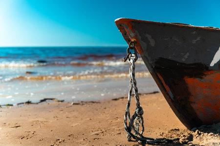 An old fishing boat secured with a chain on the sunny beachの写真素材