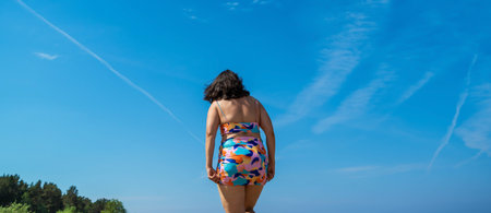 A woman walks towards a bright blue sky with white contrails