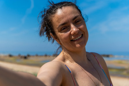 A woman smiles while taking a selfie on a beachの写真素材
