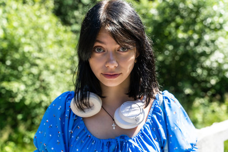 Woman with black hair in headphones and blue dress in park