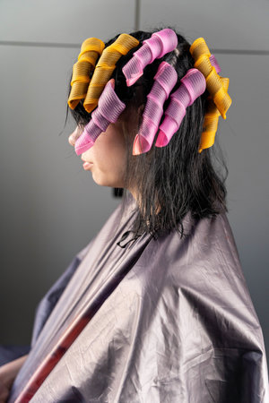 A woman in a salon cape with her hair in pink and yellow curlersの写真素材