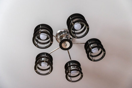 A black and chrome chandelier with five lights hangs from a white ceiling