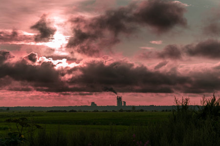 Sunset illuminates an industrial area with dark clouds and rising smokeの写真素材