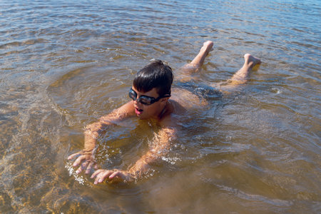 A boy swims energetically in a serene lake while wearing gogglesの写真素材