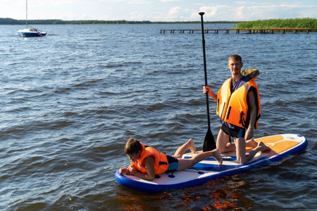 Family paddleboarding on a serene lake under a clear skyの写真素材